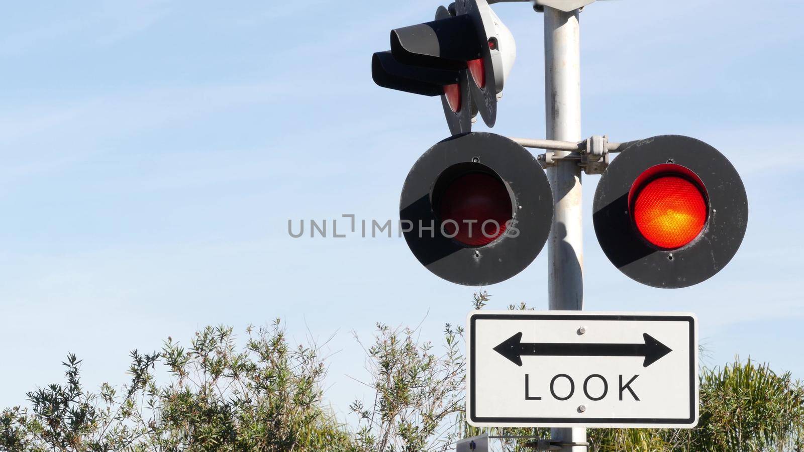 Level crossing warning signal in USA. Crossbuck notice and red traffic light on rail road intersection in California. Railway transportation safety symbol. Caution sign about hazard and train track.