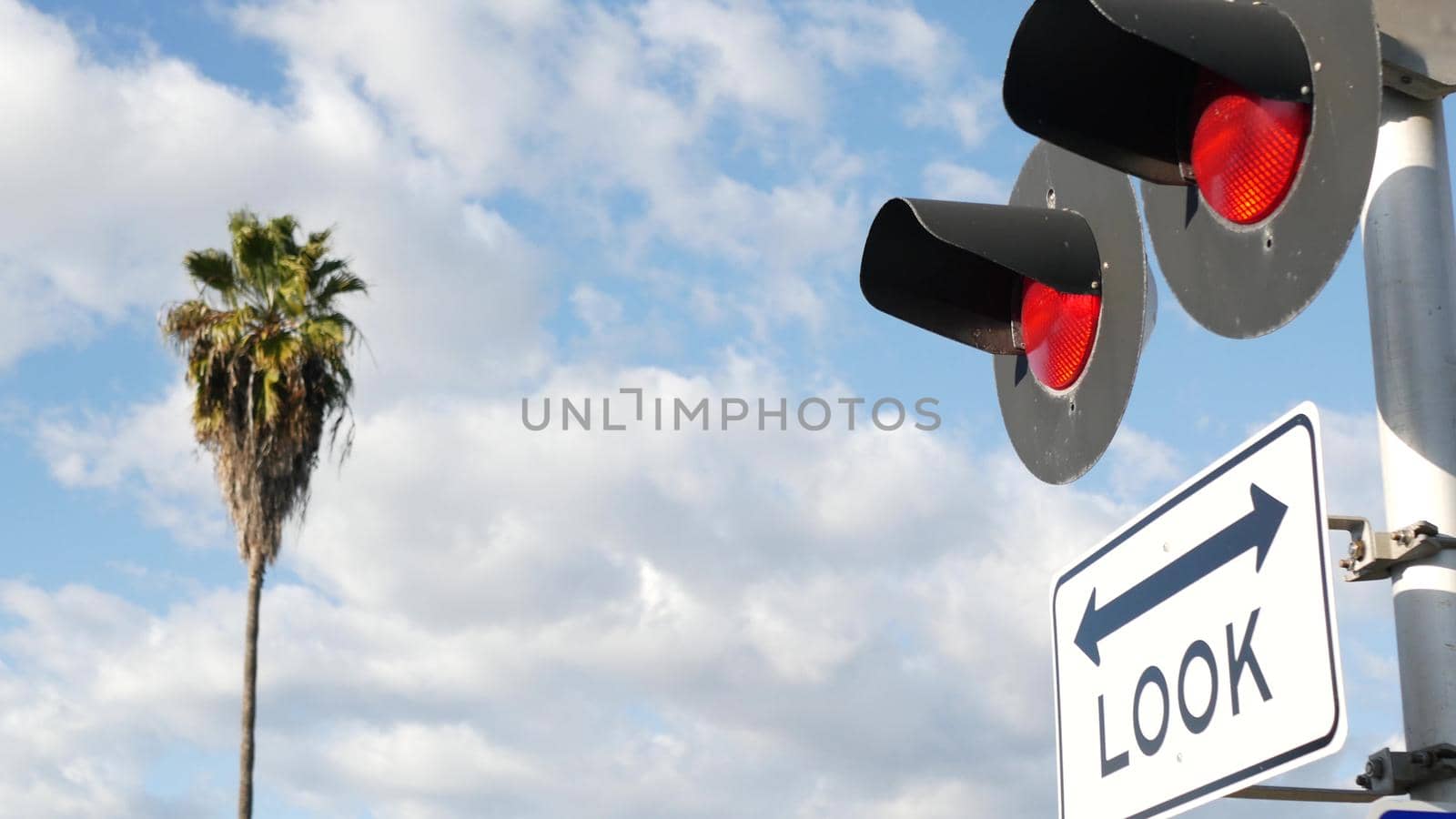Level crossing warning signal in USA. Crossbuck notice and red traffic light on rail road intersection in California. Railway transportation safety symbol. Caution sign about hazard and train track.