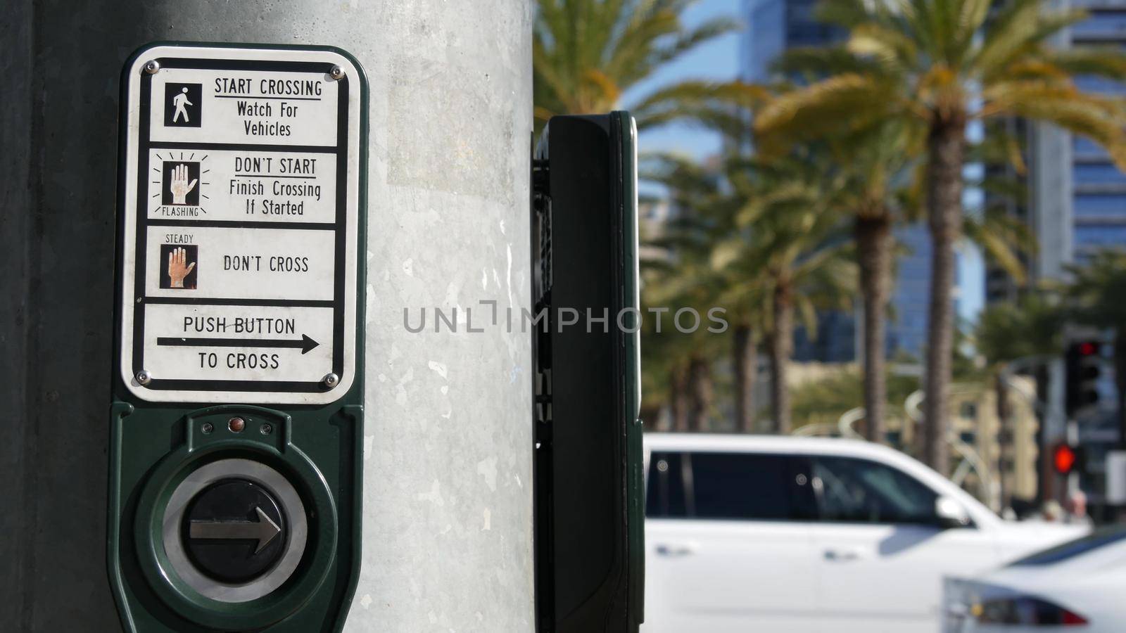 Traffic light button on pedestrian crosswalk, people have to push and wait. Traffic rules and regulations for public safety in USA. Zebra street crossing on road intesection in San Diego, California.