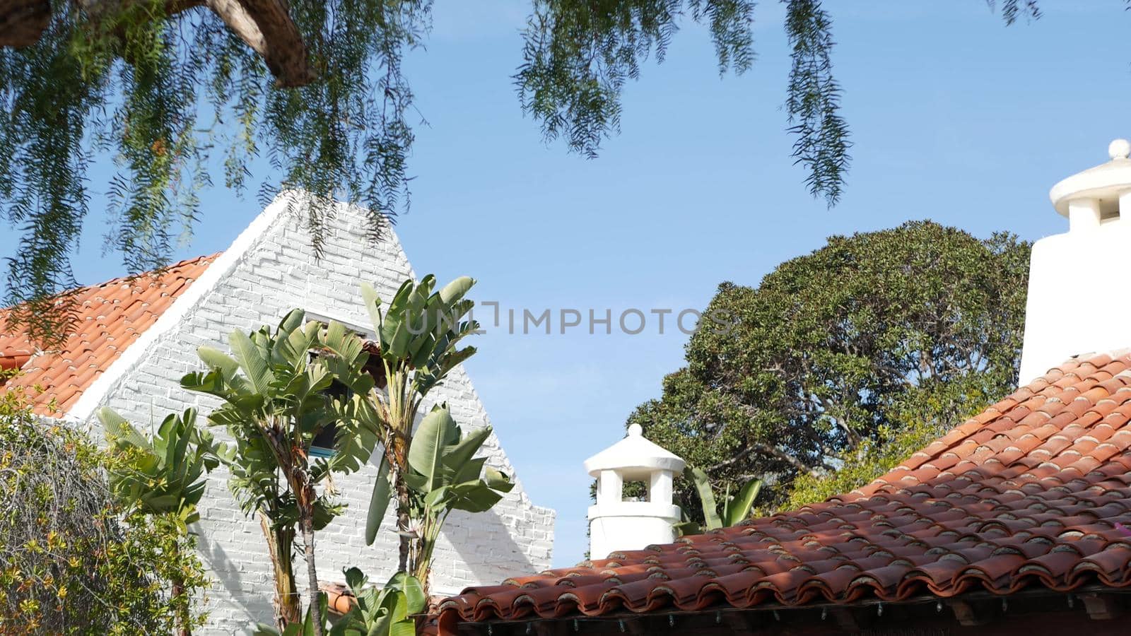 Mexican colonial style suburban, hispanic house exterior, green lush garden, San Diego, California USA. Mediterranean terracotta ceramic clay tile on roof. Rustic spanish tiled rooftop. Rural details.