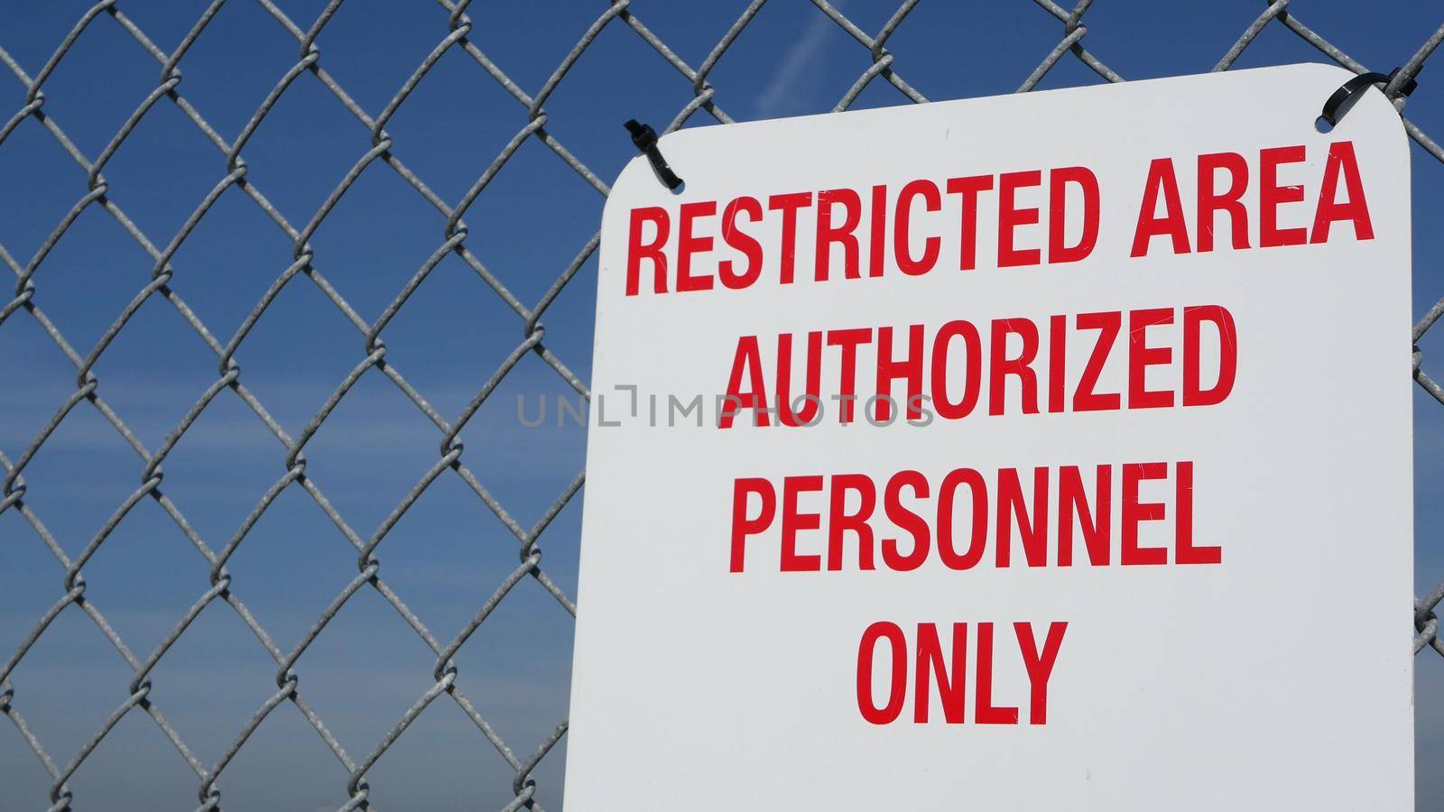 Restricted area, authorized personnel only sign in USA. Red letters, keep off warning on metal fence, United States border symbol. No trespassing notice means violators will be prosecuted by US law.