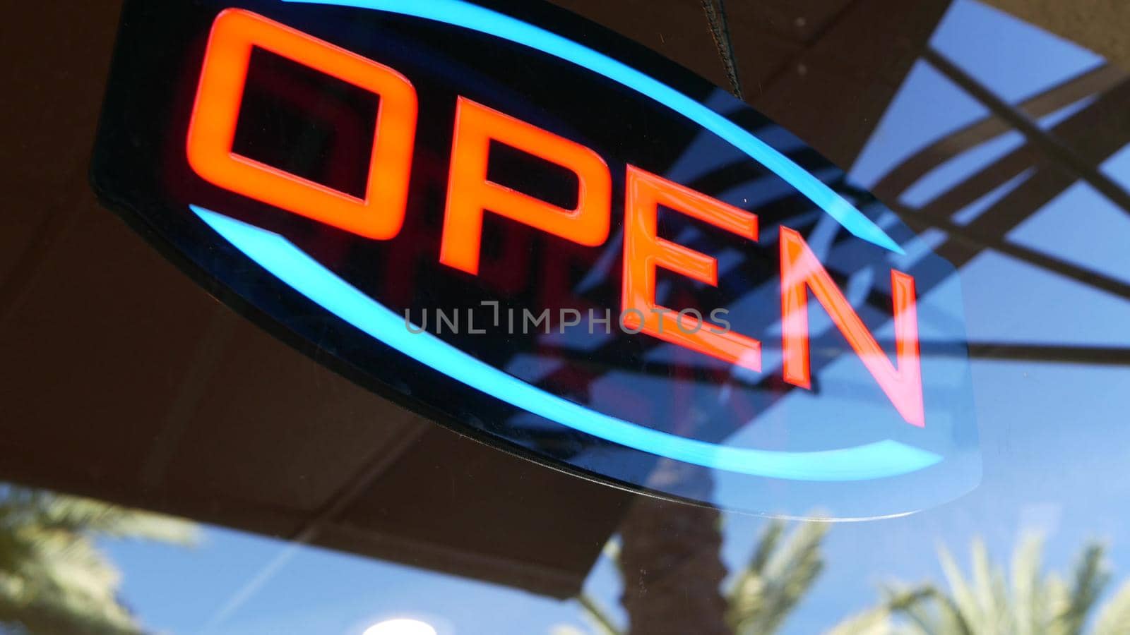 Open neon sign glowing in the dark. Vivid retro styled text at entrance on glass window. Colorful electric banner selective focus close up. Light bulbs radiance at night. Shiny illuminated lettering.