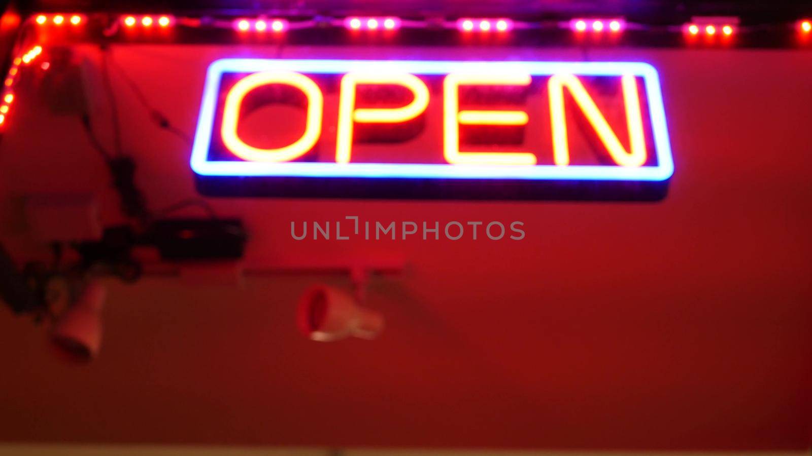 Open neon sign glowing in the dark. Vivid retro styled text at entrance on glass window. Colorful electric banner selective focus close up. Light bulbs radiance at night. Shiny illuminated lettering.