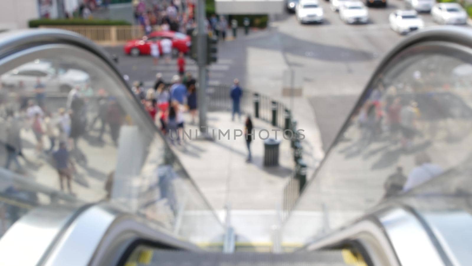 Perspective view thru escalator, defocused unrecognizable group of people on road intersection crosswalk on Strip of Las Vegas, USA. Anonymous blurred pedestrians on walkway in crowded urban downtown.