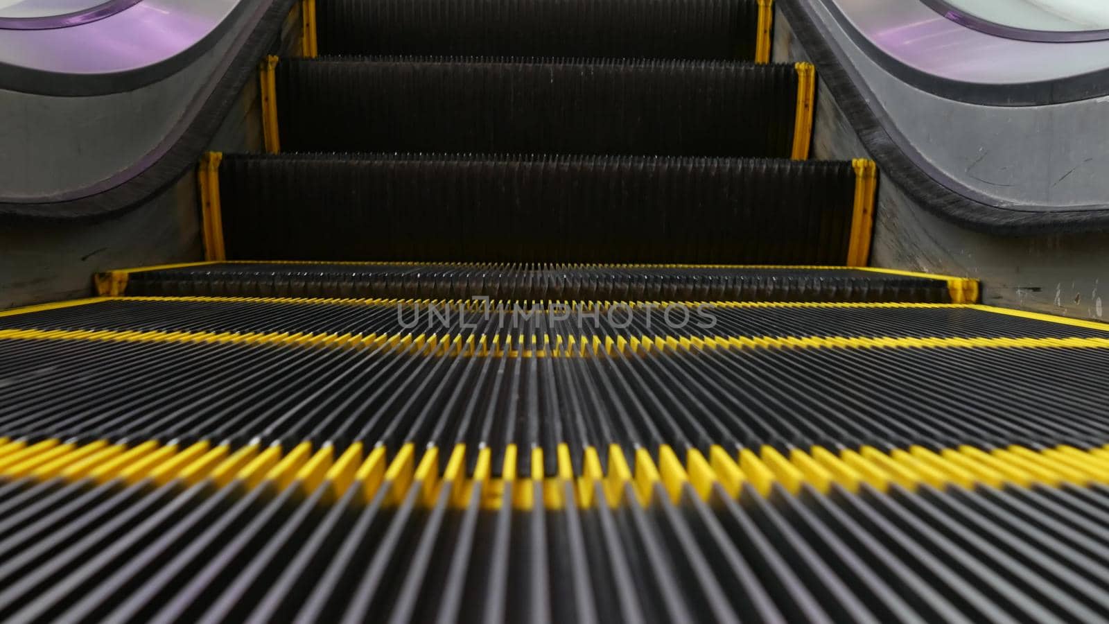 Low angle looped perspective view of modern escalator stairs. Automated elevator mechanism. Yellow line on stairway illuminated with purple light. Futuristic empty machinery staircase moving straight.