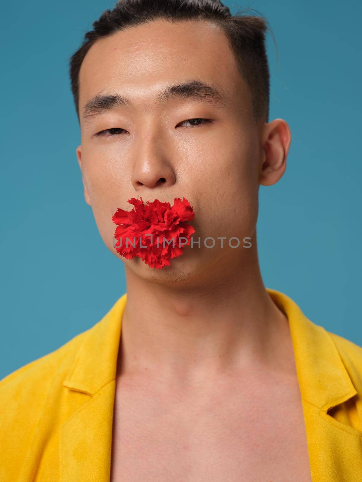 The guy is Korean appearance with a flower in his mouth on a blue background and a yellow jacket. High quality photo