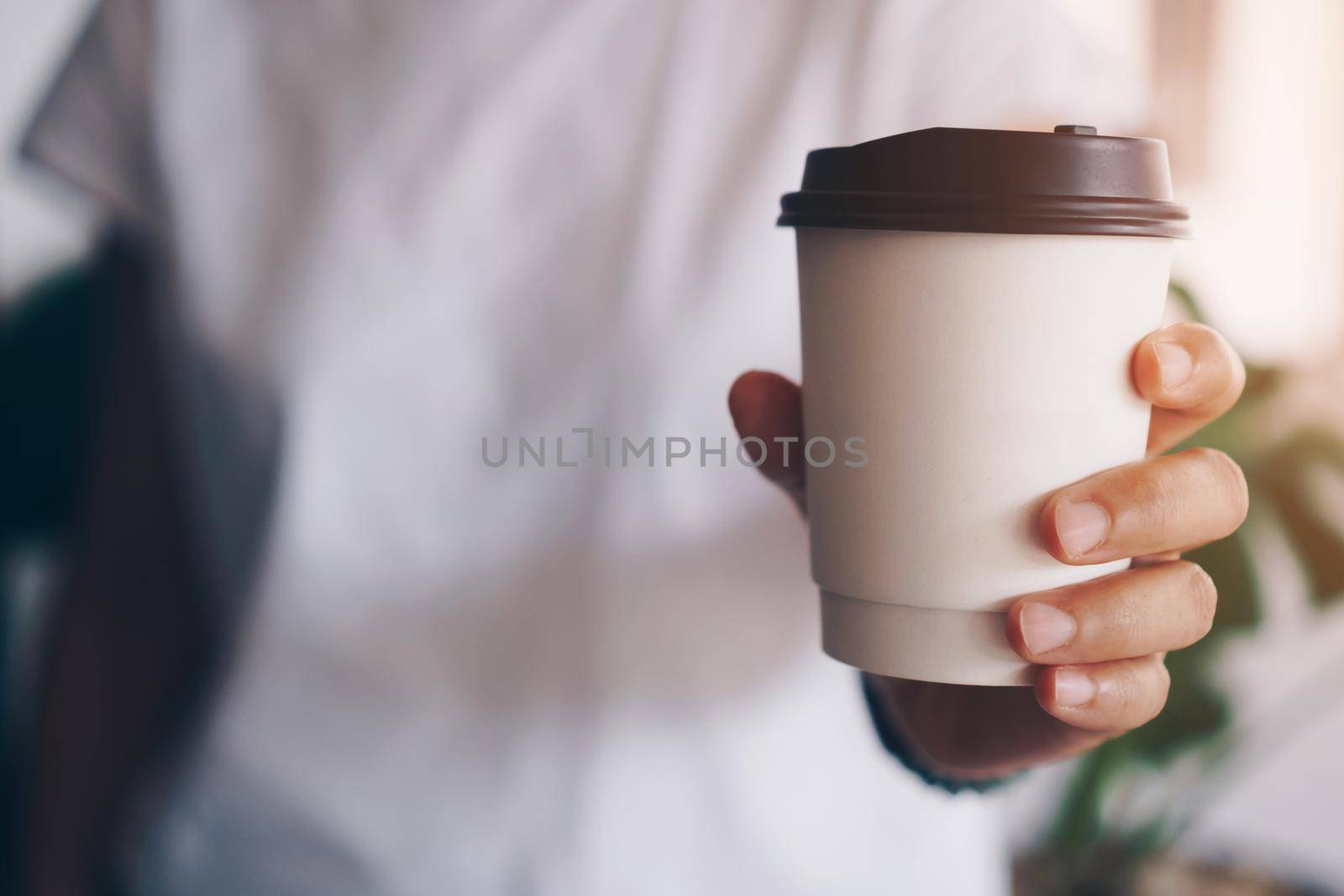 Hand hold a cup of coffee with sunlight flare beautiful copy space background. Wake up caffeine intake in morning. by Suwant