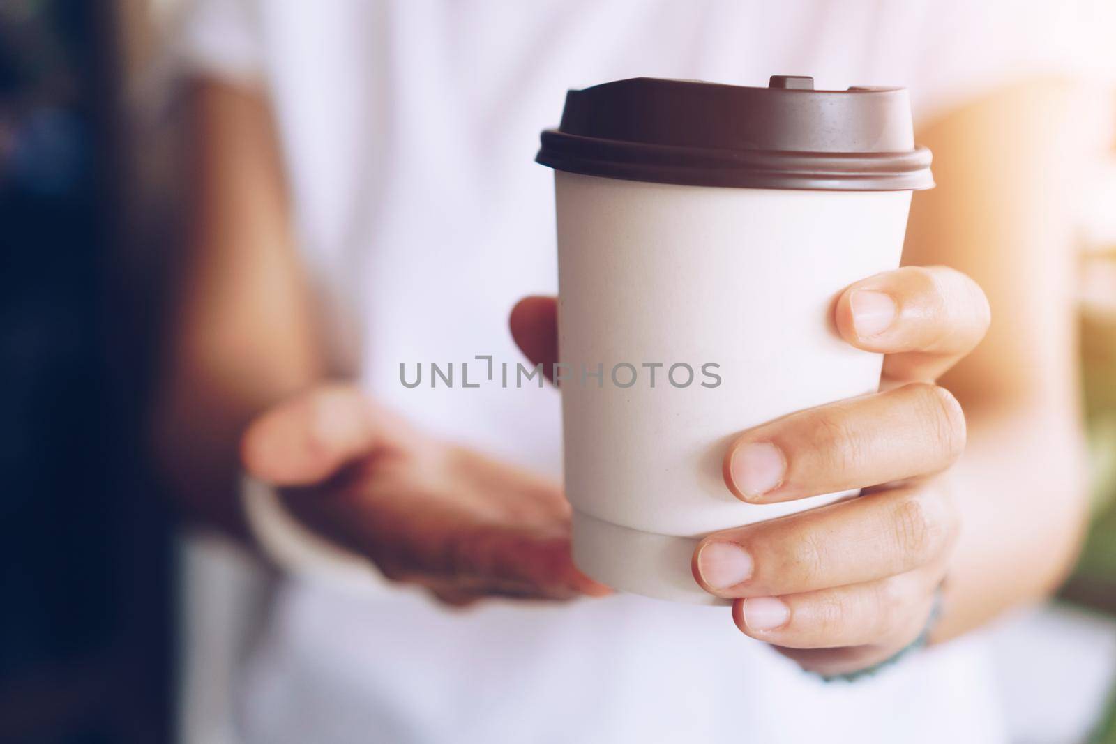 Hand hold a cup of coffee with sunlight flare beautiful copy space background. Wake up caffeine intake in morning time.