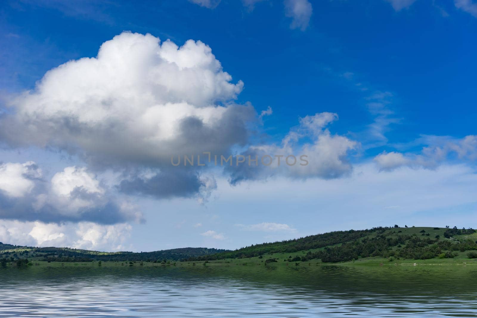 Natural landscape with a green field covered with grass under the blue sky with clouds.