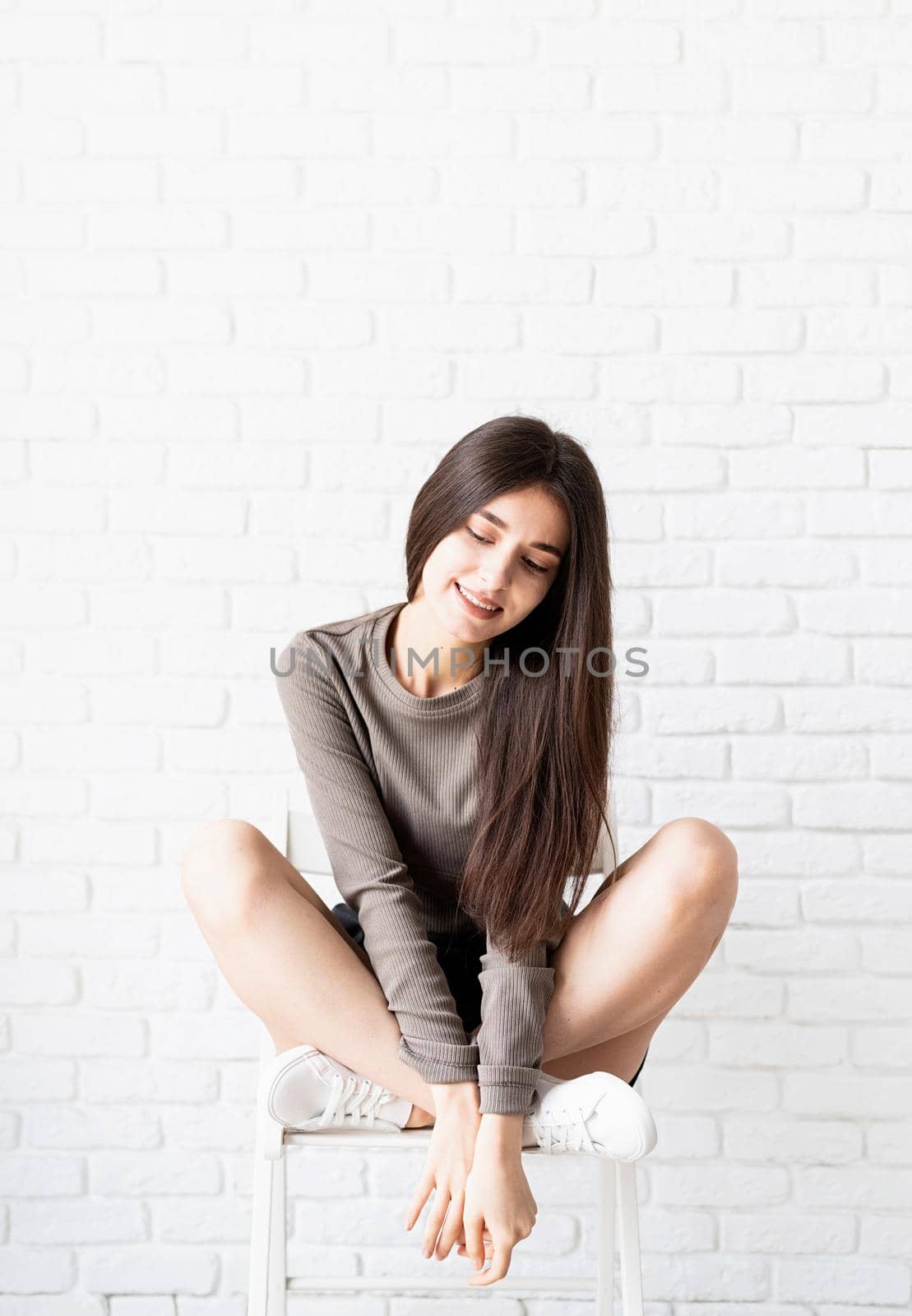 portrait of a beautiful brunette woman with long hair sitting on white brick wall background, thinking by Desperada