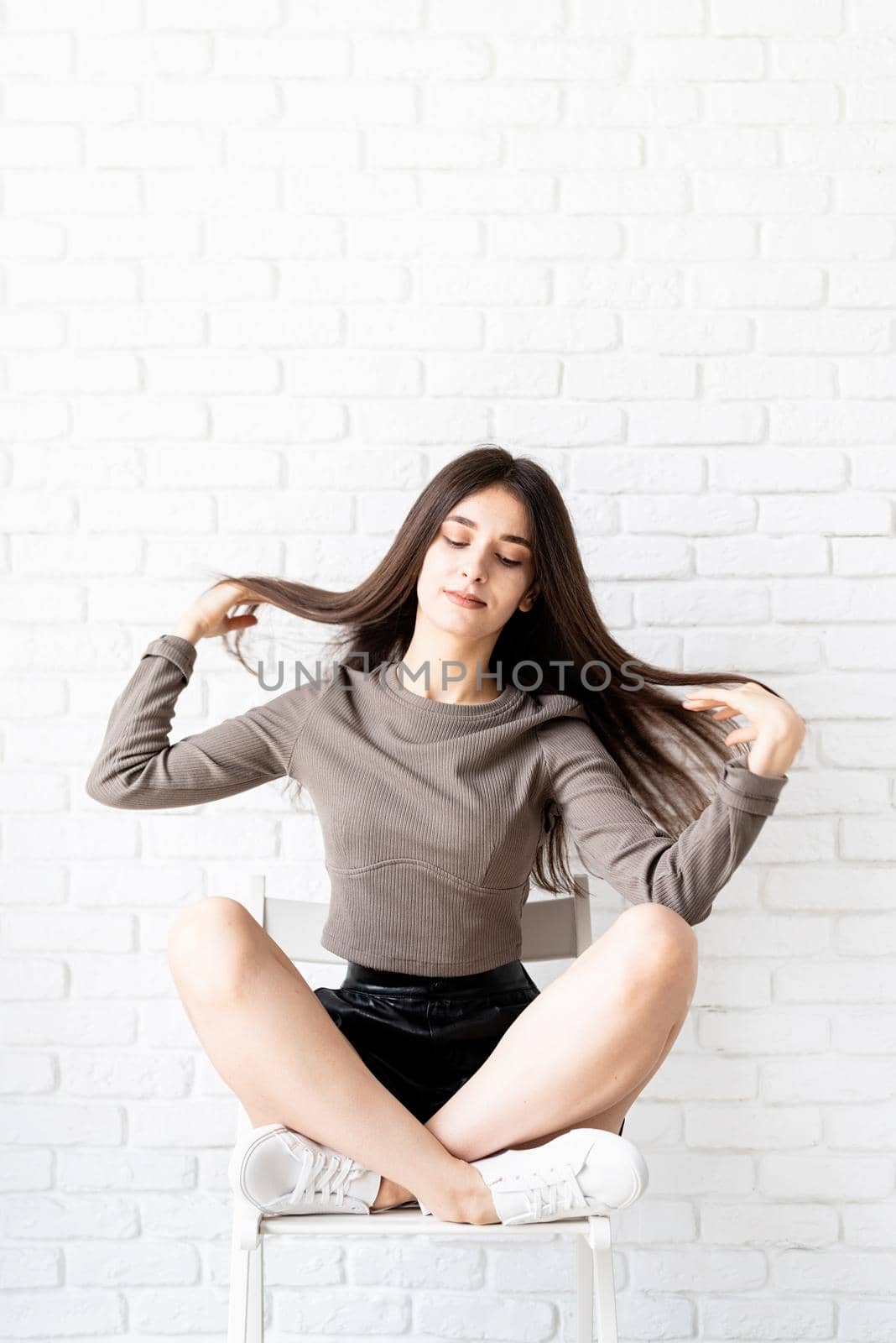 portrait of a beautiful brunette woman with long hair sitting on white brick wall background by Desperada