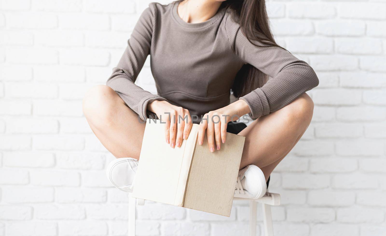 Woman in brown shirt sitting on the chair with legs crossed holding an opened book