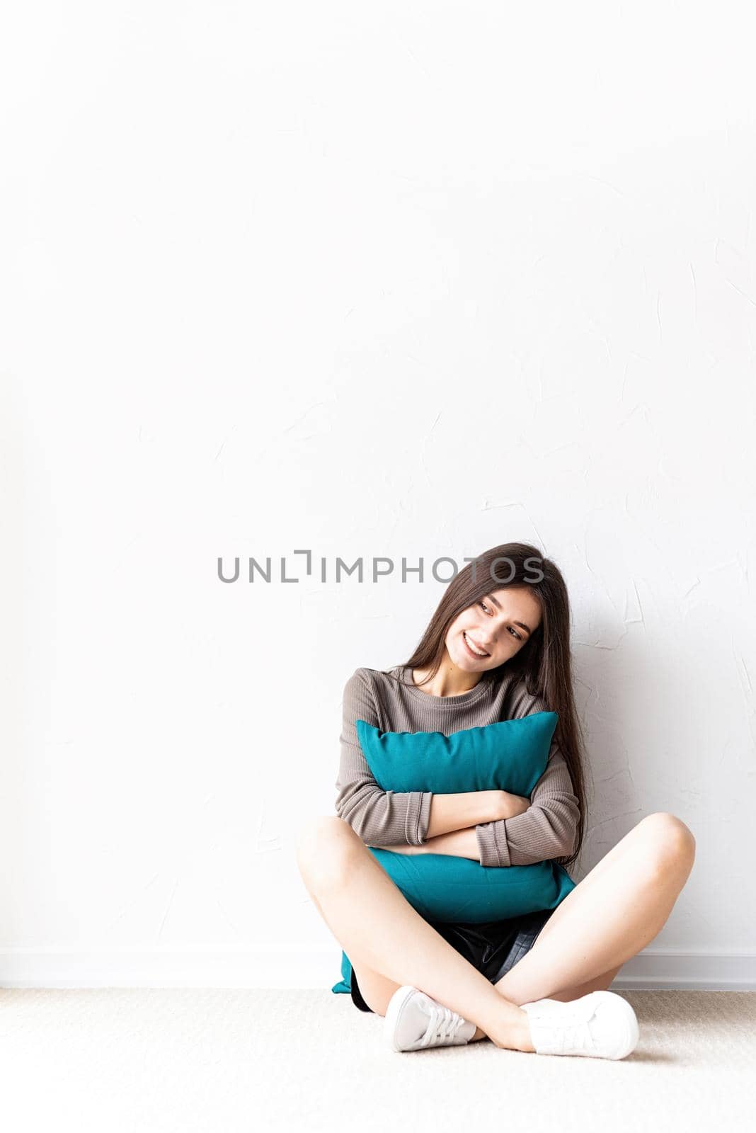 Beautiful young woman in casual clothes sitting on the floor with pillows smiling looking away