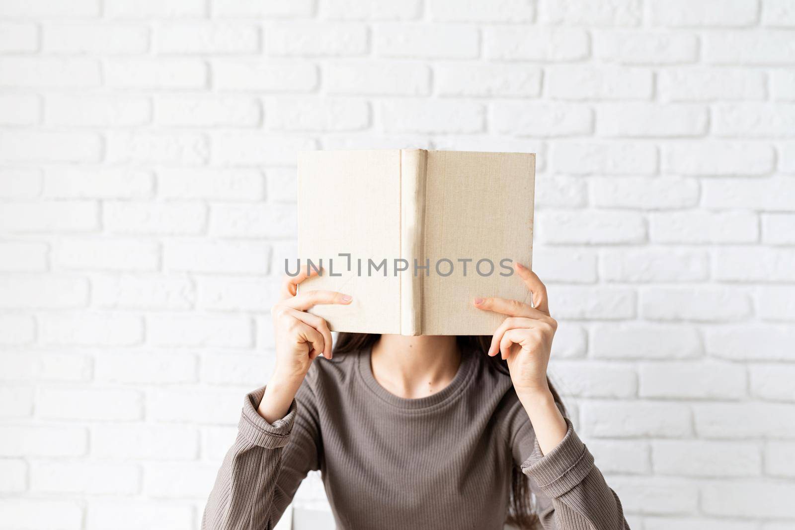 Woman in brown shirt holding an opened book in front of her face