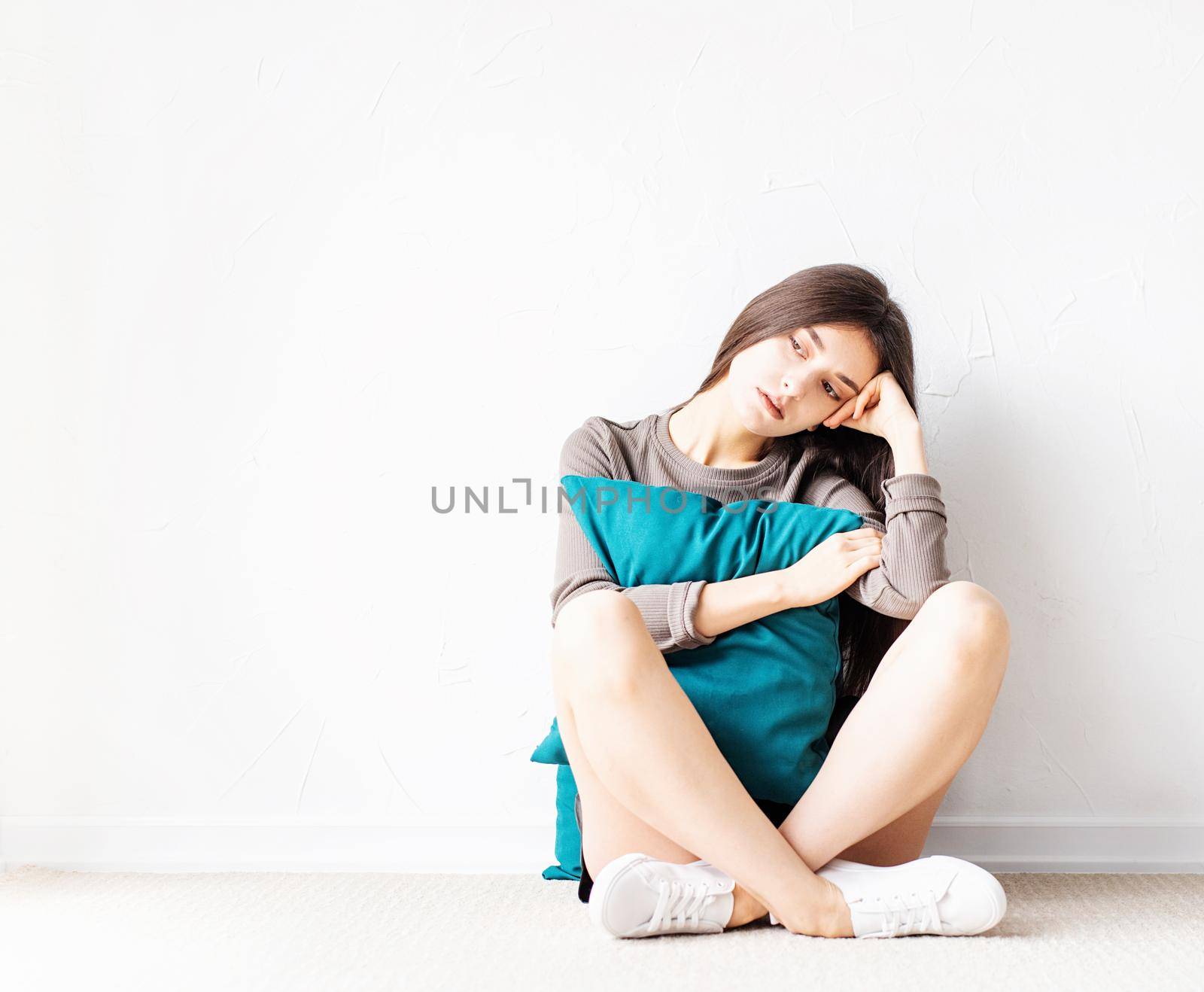 Mental health concept. Beautiful sad woman in brown shirt and black leather shorts sitting on the floor with pillow deep in thought