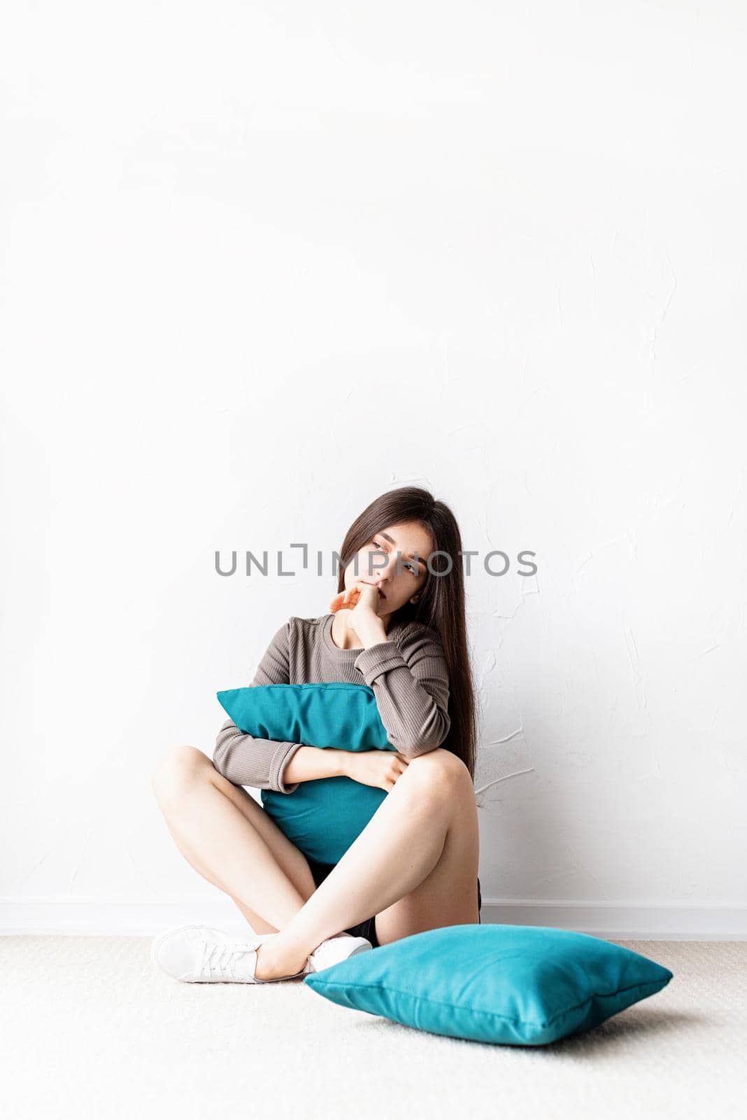 Mental health concept. Beautiful sad woman in brown shirt and black leather shorts sitting on the floor with pillow deep in thought