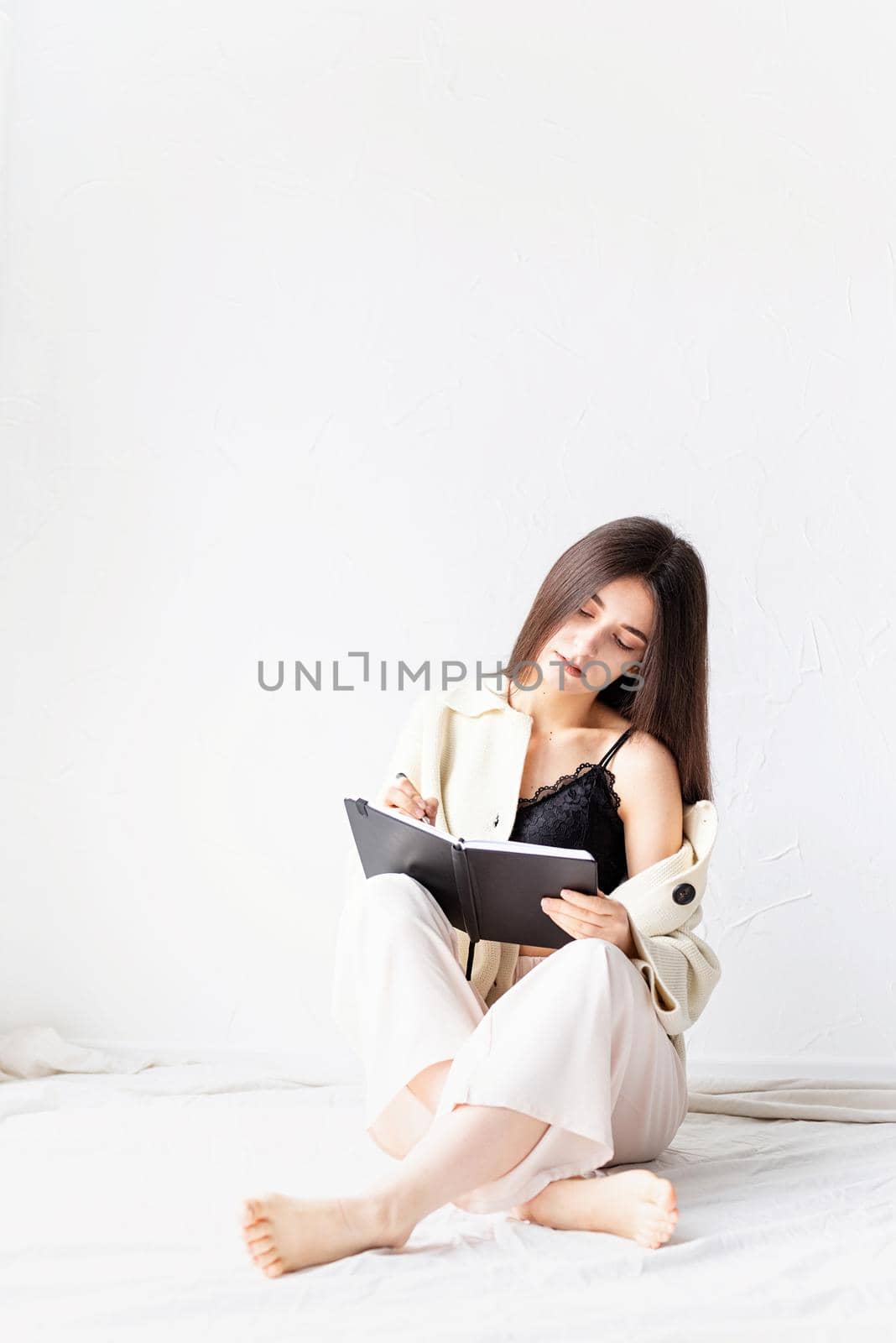Beautiful woman in comfy home clothes writing notes sitting on the floor by Desperada