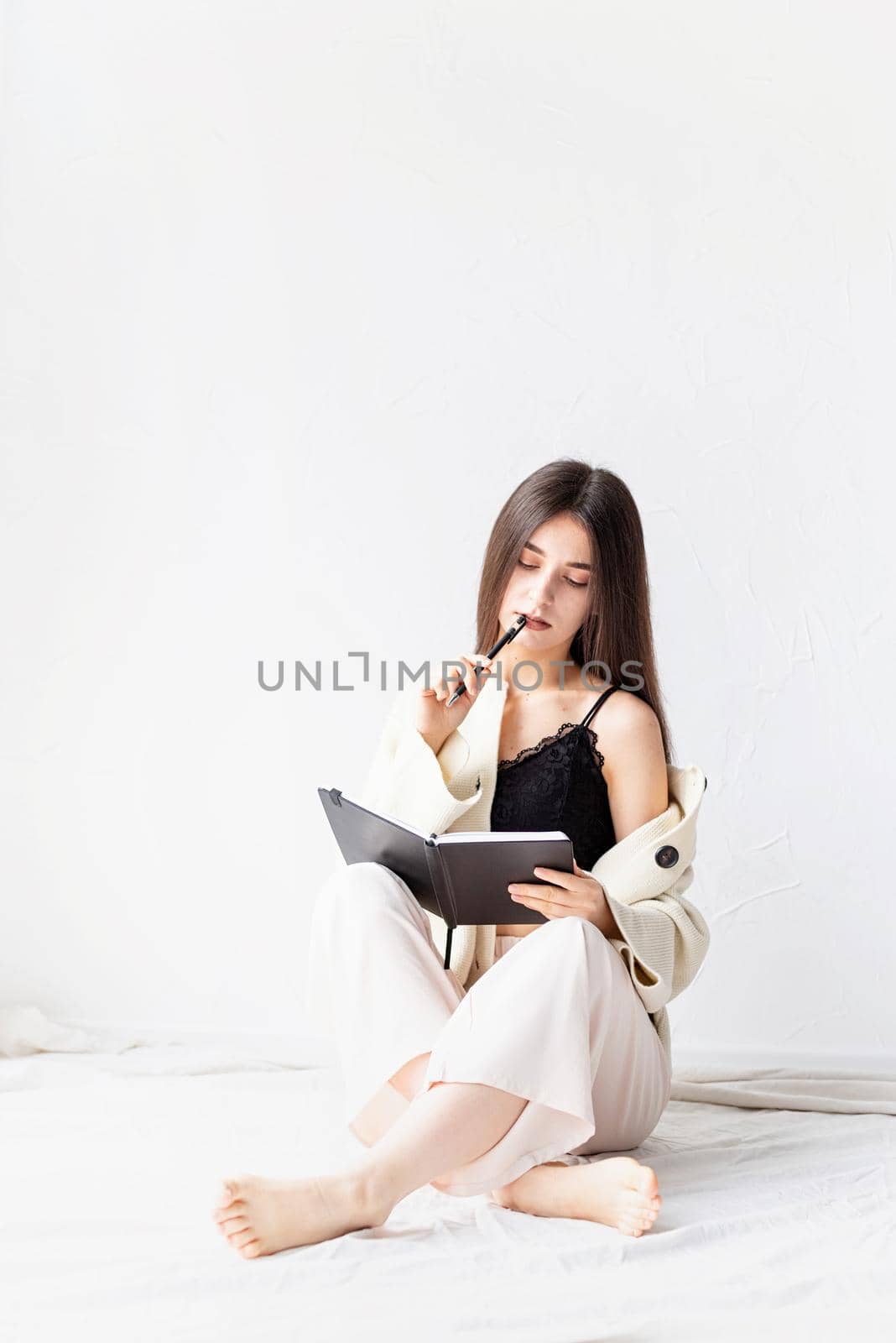 Beautiful sexy woman in comfy home clothes writing notes sitting on the floor, thinking