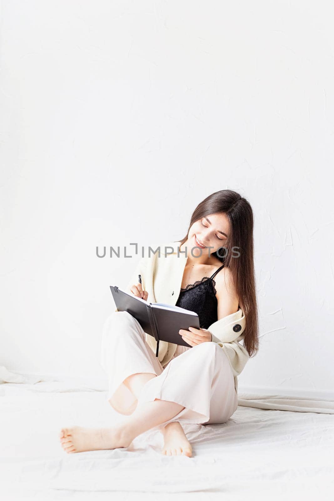 Beautiful woman in comfy home clothes writing notes sitting on the floor by Desperada