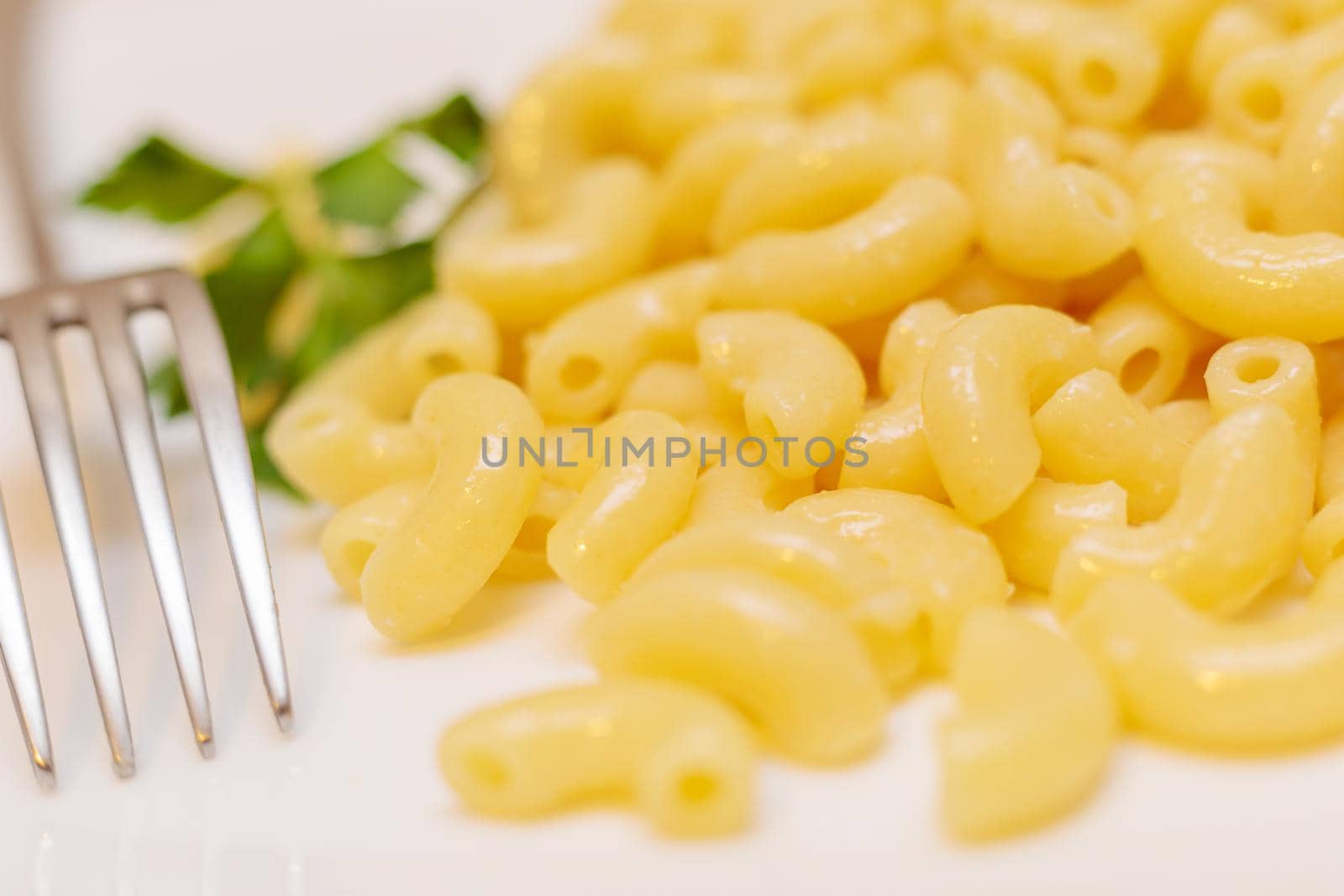 Boiled yellow pasta on a white plate with a fork. Close-up.
