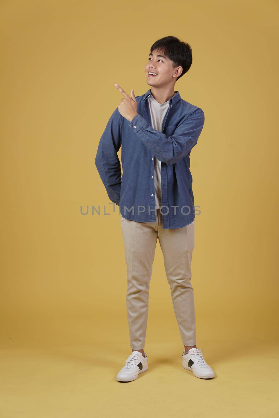 portrait of happy handsome young asian man dressed casually pointing fingers at copyspace isolated on yellow studio background