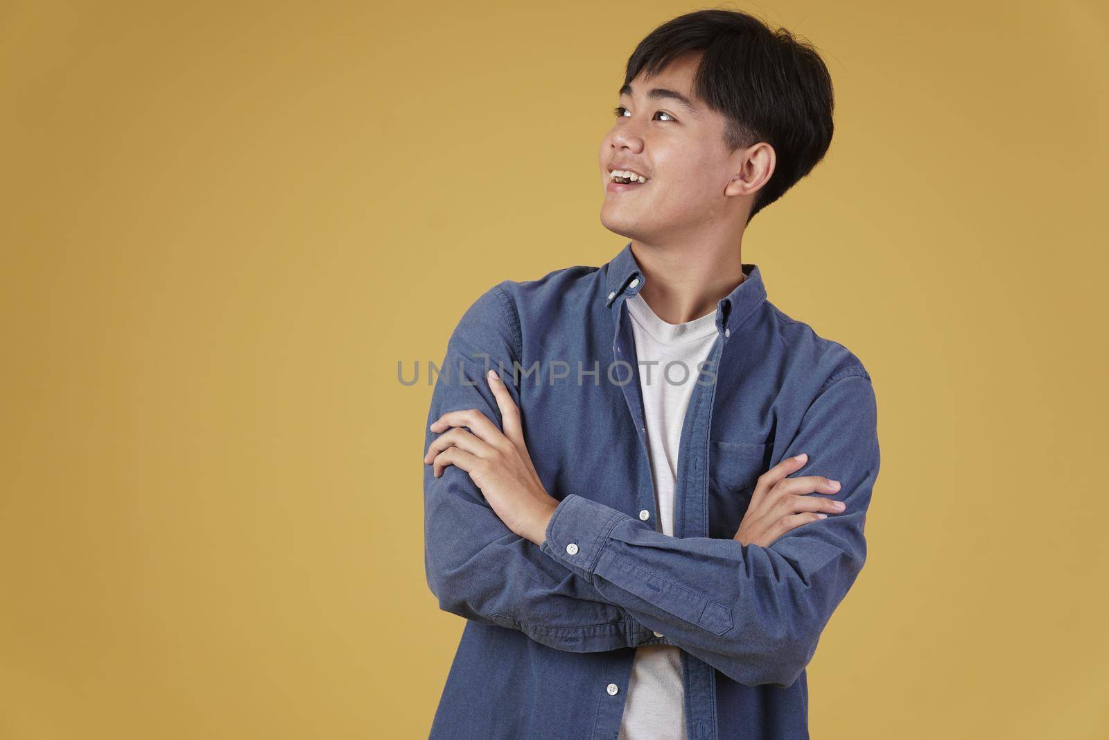 portrait of happy handsome young asian man dressed casually with folded crossed arms gesture isolated on yellow studio background
