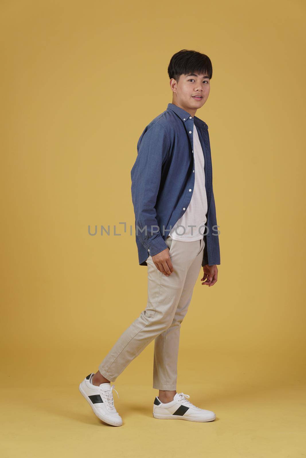 portrait of handsome young asian man dressed casually isolated smiling walking on yellow studio background