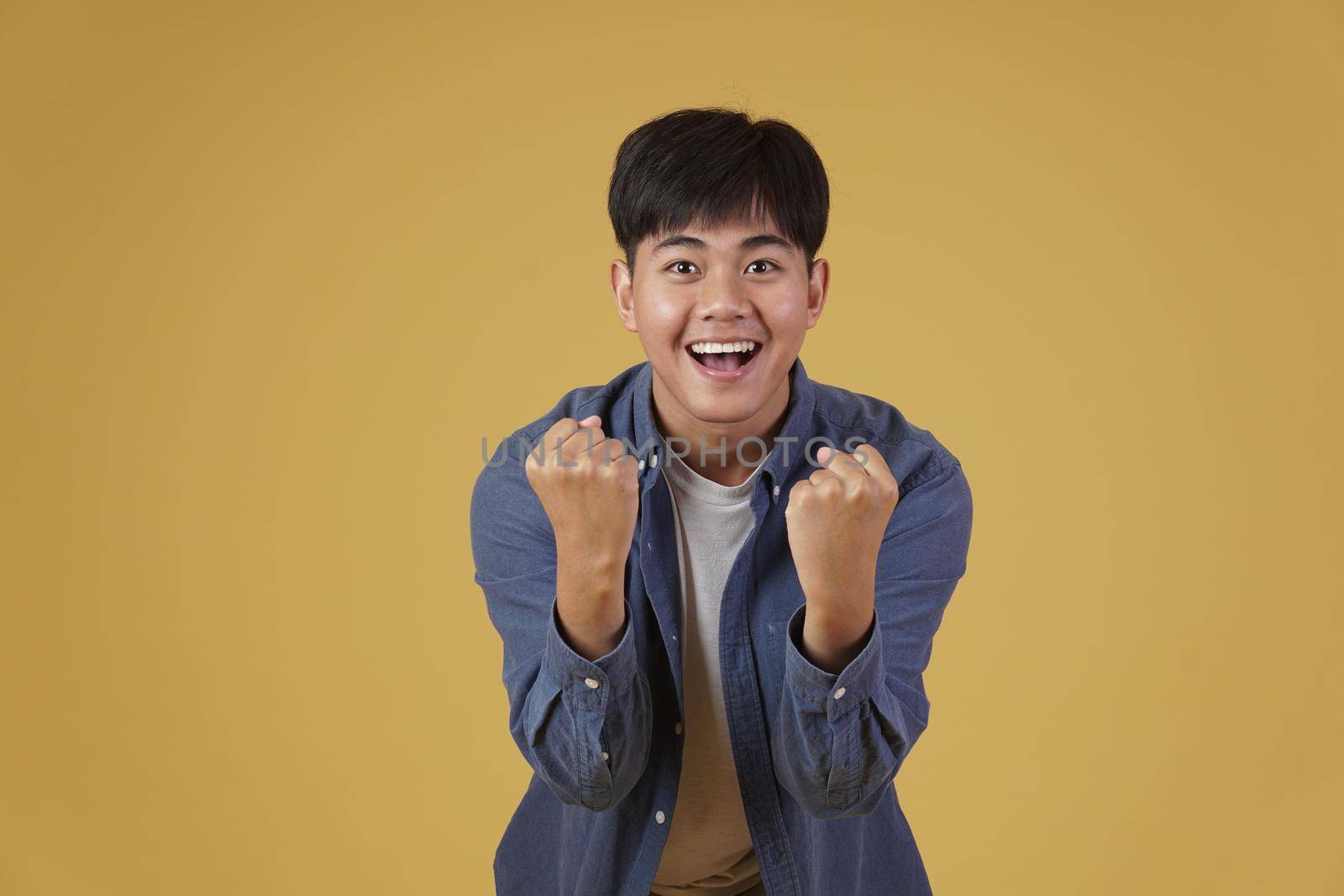 portrait of  glad cheerful happy rejoicing excited overjoyed young asian man dressed casually isolated on yellow studio background
