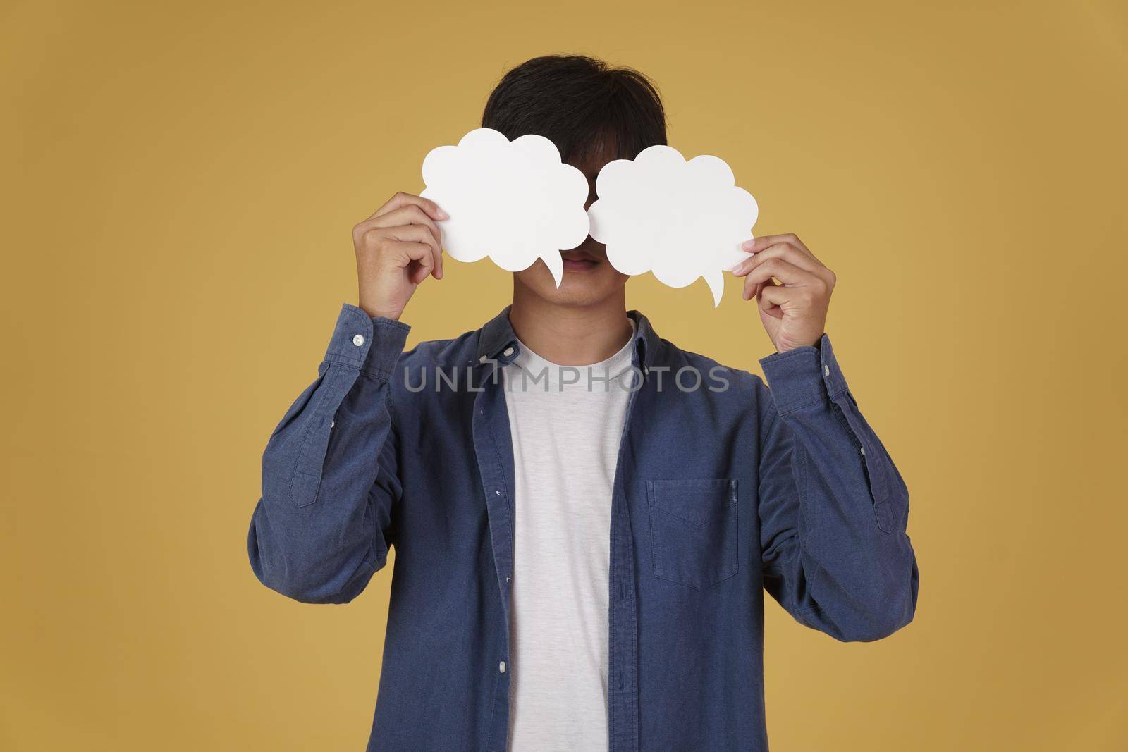 portrait of smiling happy cheerful young asian man dressed casually with empty speech bubble isolated on yellow studio background