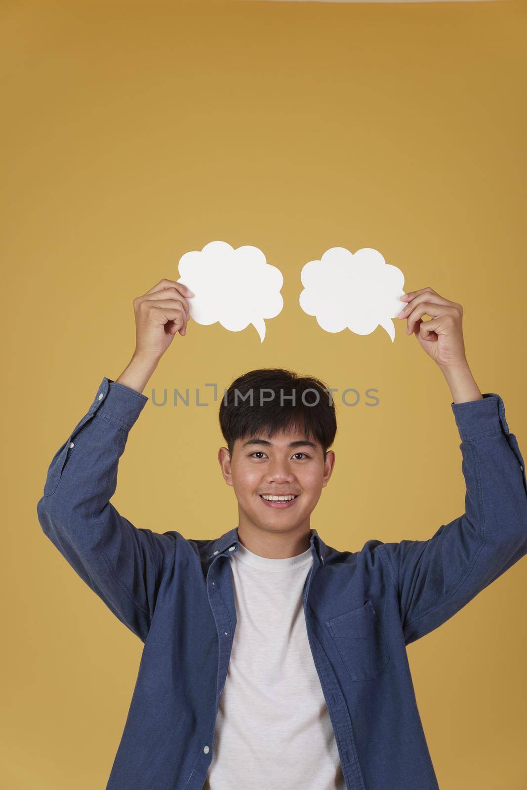 portrait of smiling happy cheerful young asian man dressed casually with empty speech bubble isolated on yellow studio background