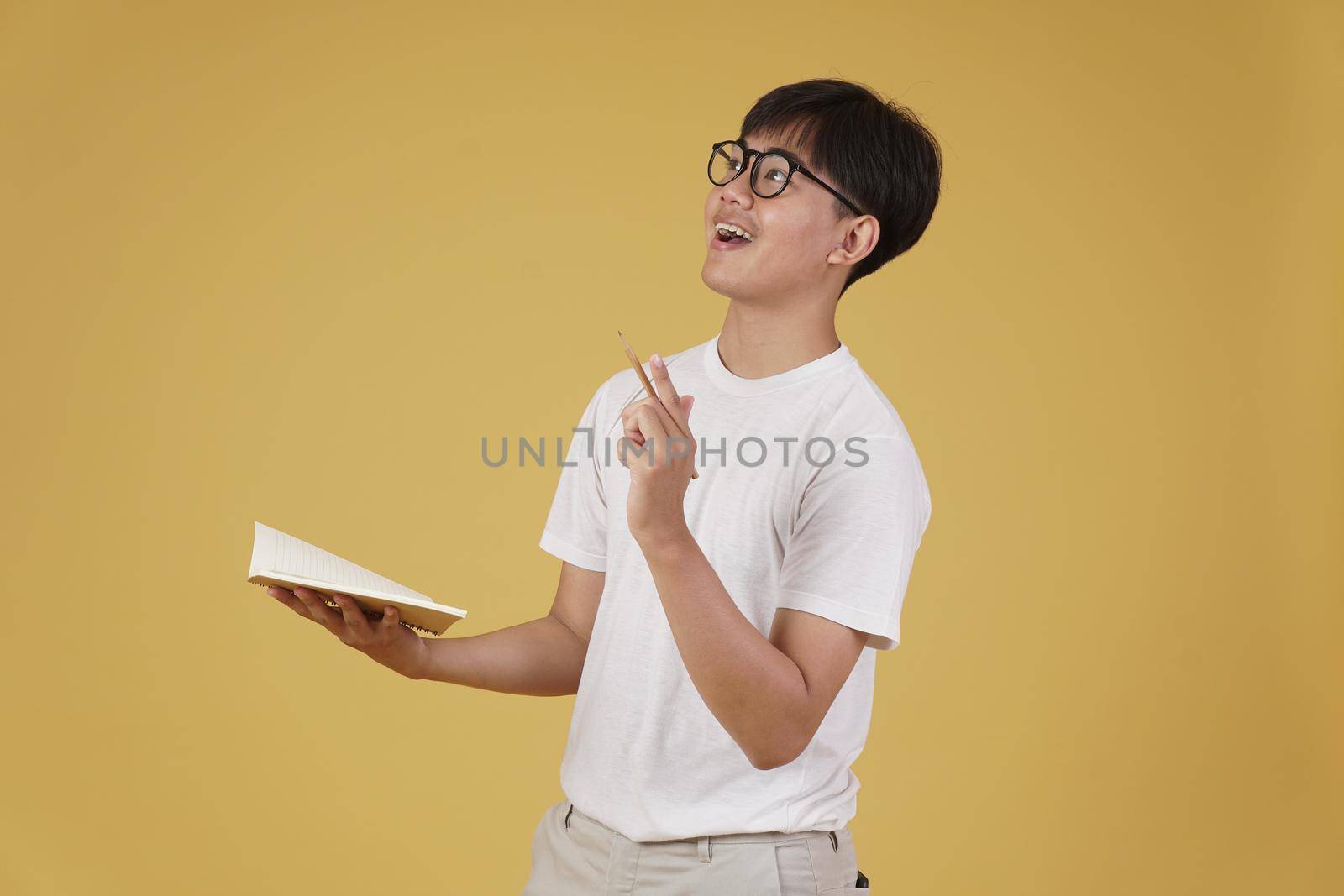 happy cheerful young asian man student dressed casually wearing eyeglasses pointing finger up having idea isolated on yellow studio background