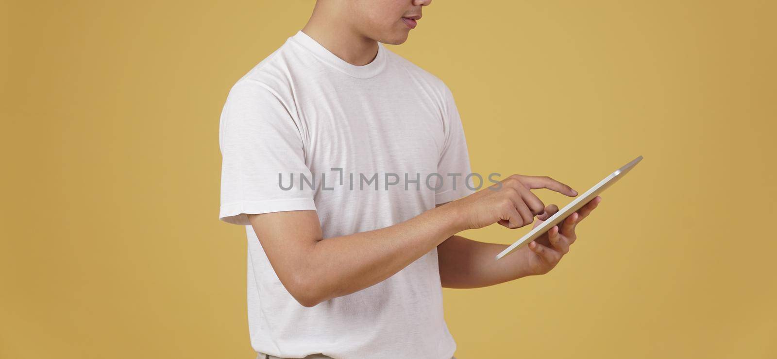 young asian man dressed casually using digital tablet isolated on yellow studio background.