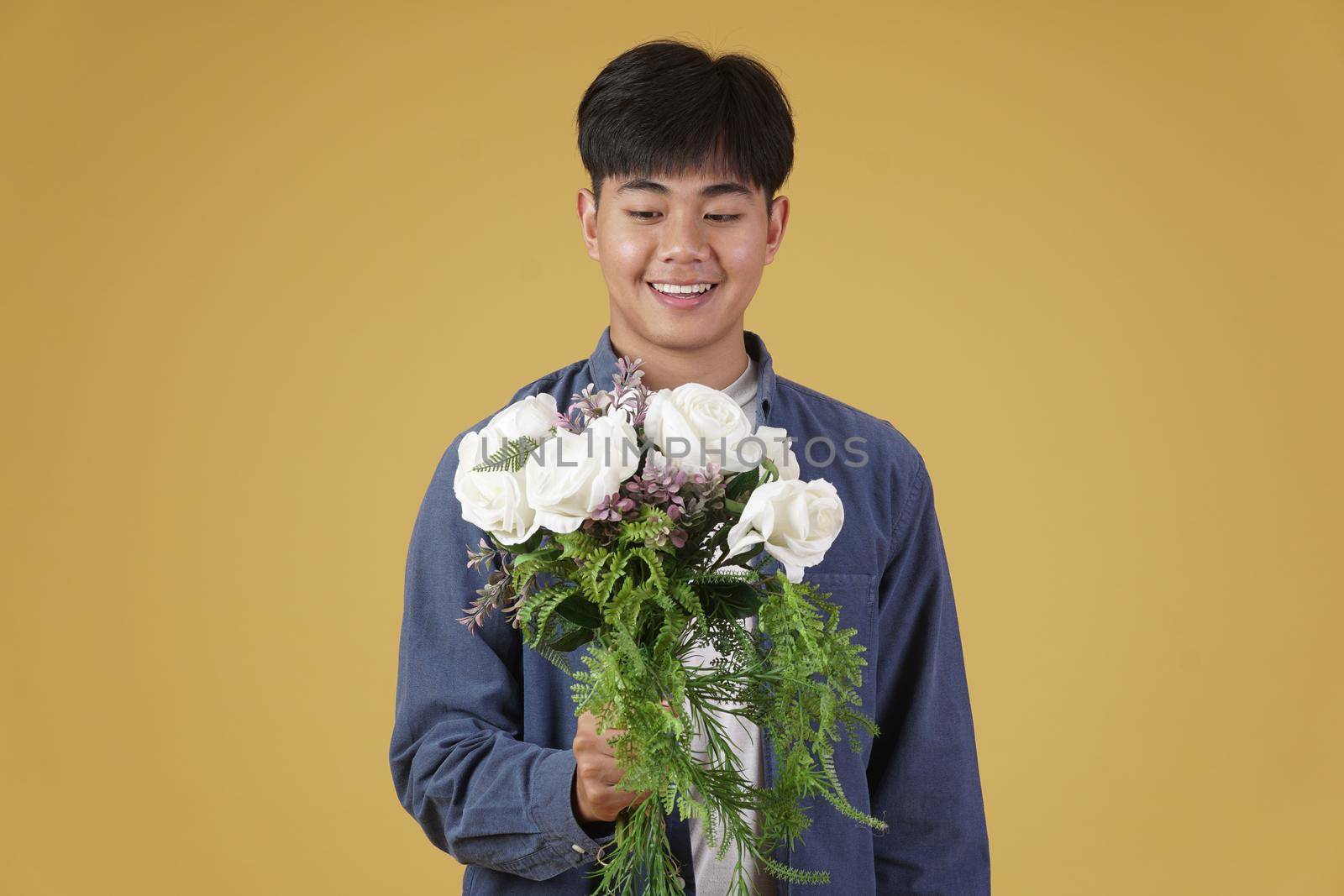 smiling happy cheerful young asian man dressed casually holding flower bouquet isolated on yellow studio background.