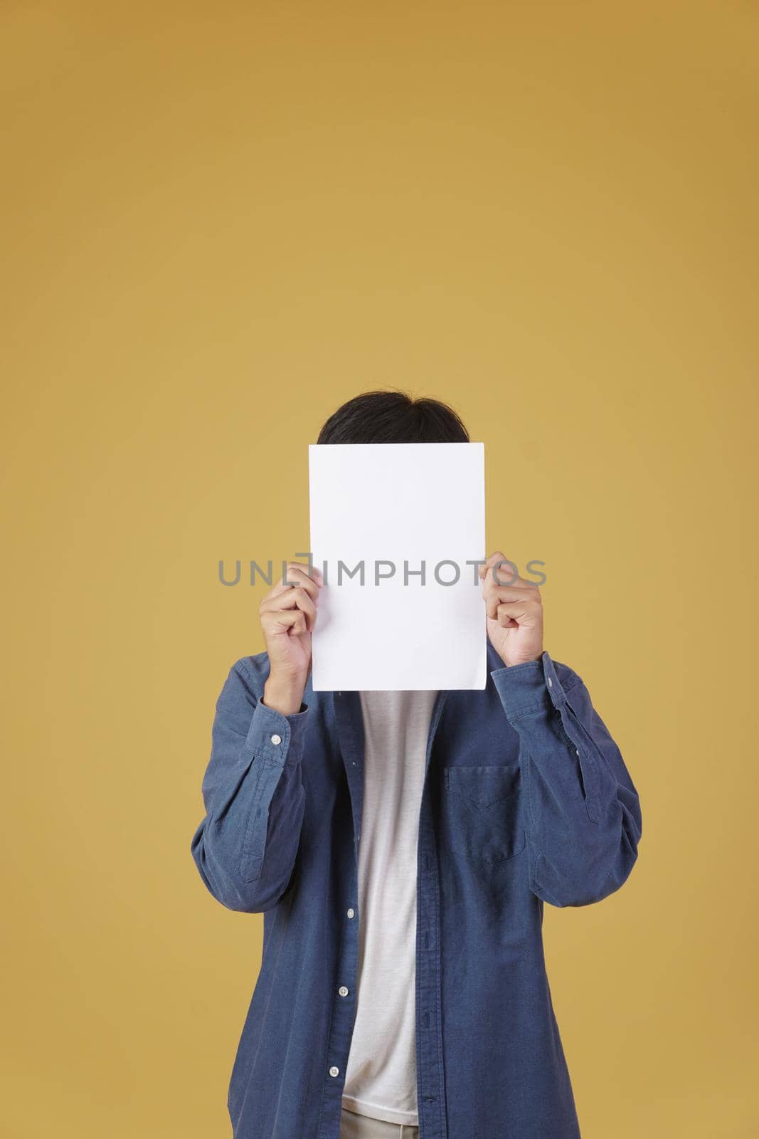 portrait of young asian man dressed casually showing blank empty placard paper isolated on yellow studio background.