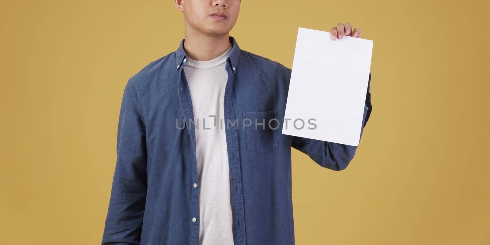 young asian man dressed casually showing blank empty placard paper isolated on yellow background. by pp99