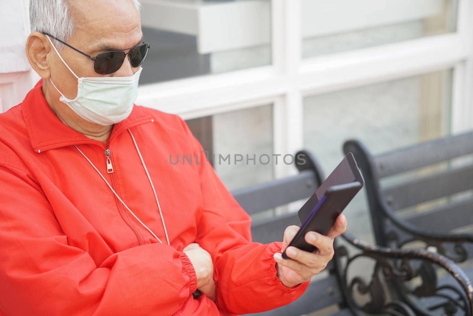 asian old elder senior man elderly male wearing face mask using mobile smart phone cellphone outdoor. mature retirement lifestyle