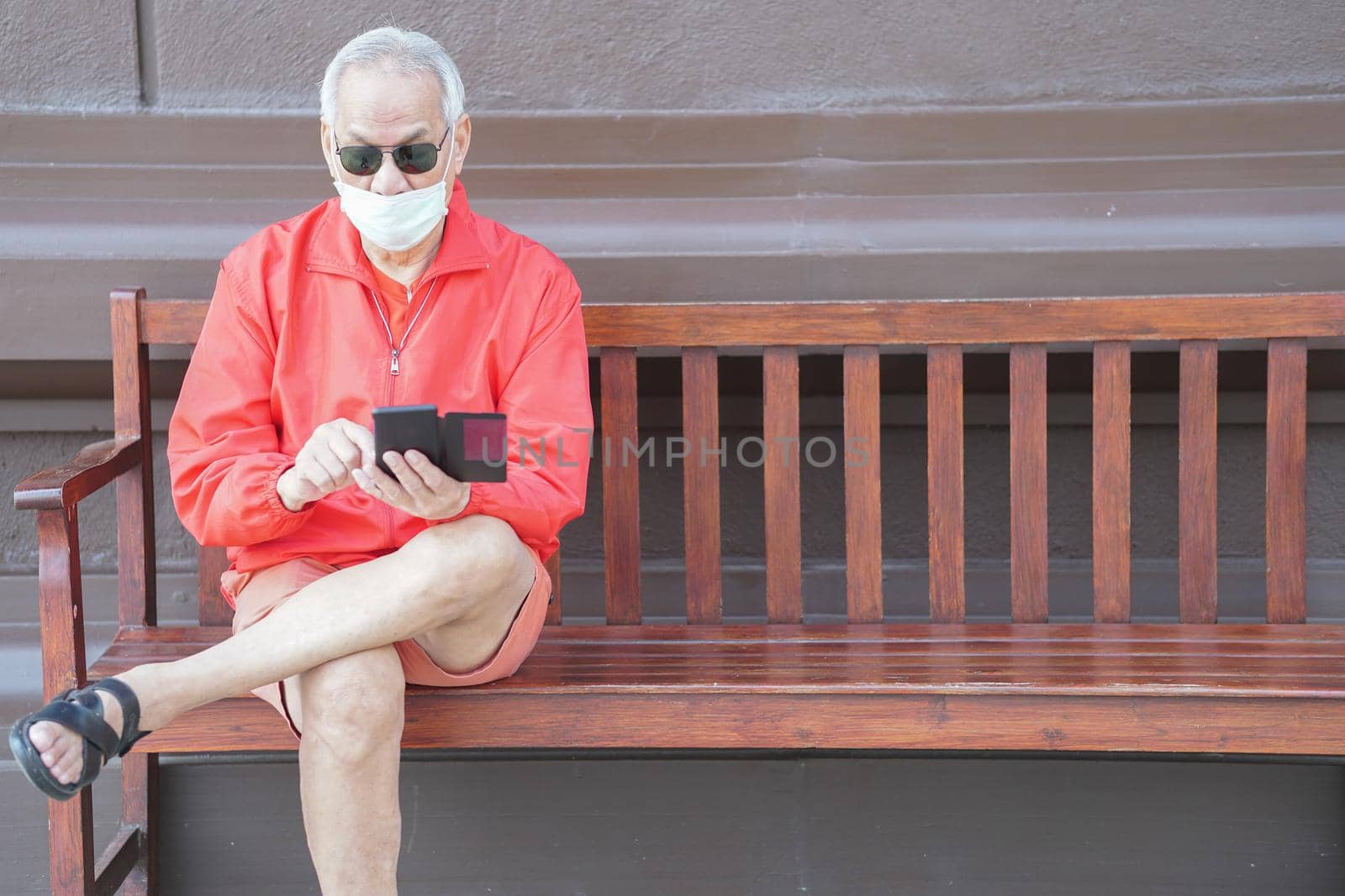 asian old elder senior man elderly male wearing face mask using mobile smart phone cellphone outdoor. mature retirement lifestyle