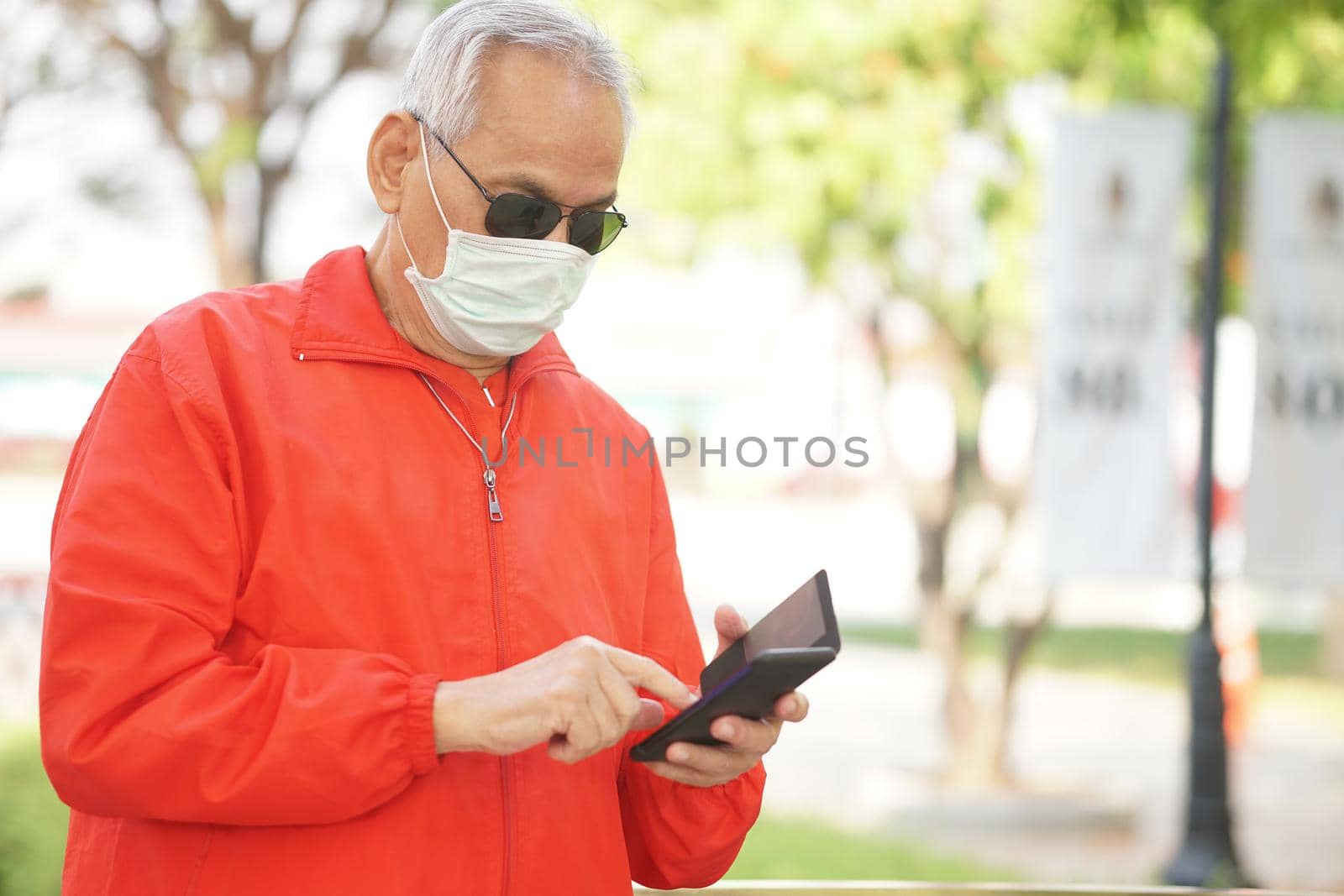 asian old elder senior man elderly male wearing face mask using mobile smart phone cellphone outdoor. mature retirement lifestyle