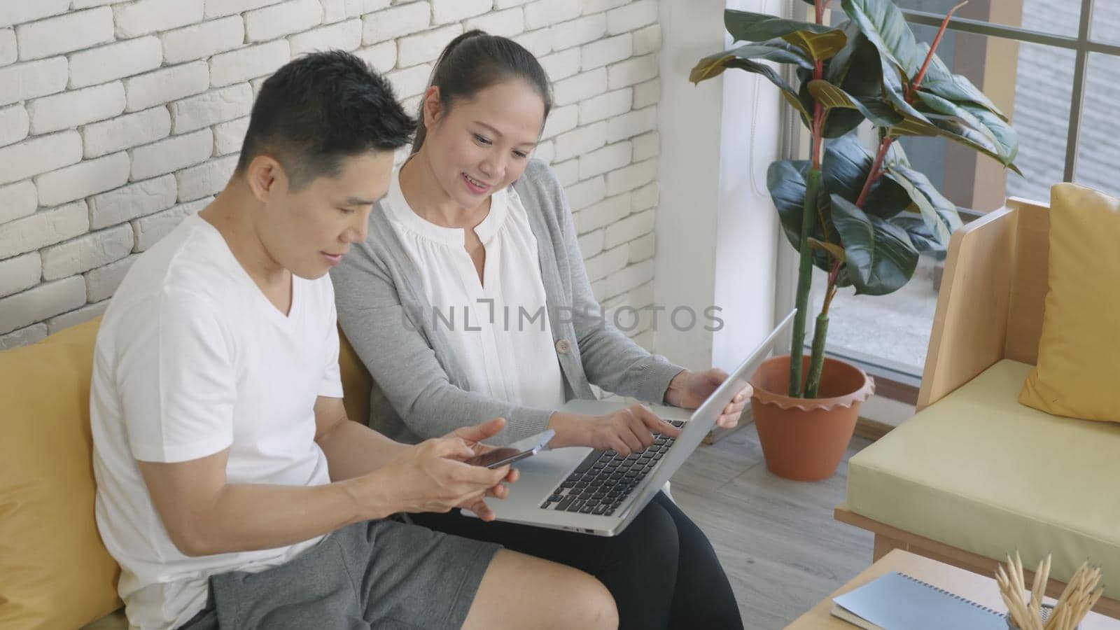 Happy Asian family couple husband and wife work and using laptop computer analyzing their finances discuss. Cheerful loving couple smile shopping order products online together from home by computer
