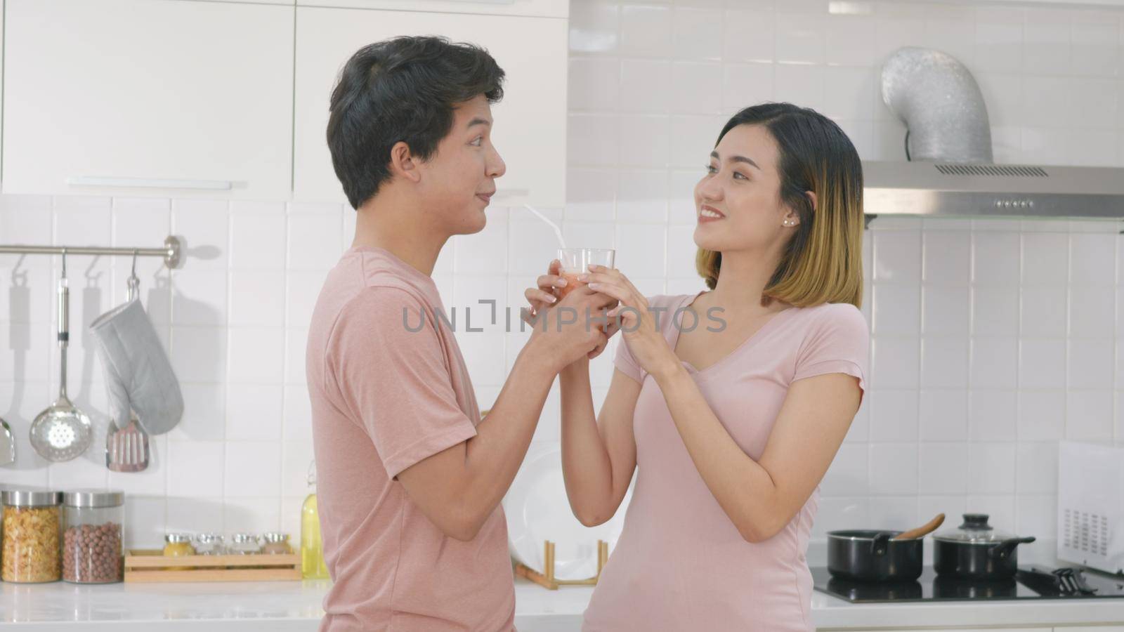 Happy Asian beautiful young family couple husband and wife enjoying drinking fresh apple smoothie juice in kitchen together at home. woman poured juice from blender for man to drink. Healthy lifestyle