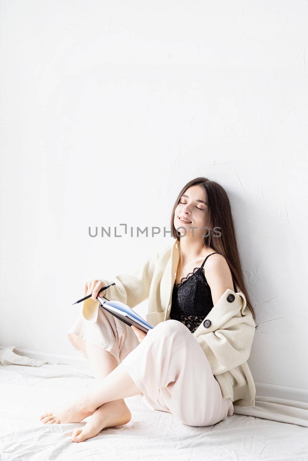 Beautiful woman in comfy home clothes writing notes sitting on the floor dreaming by Desperada