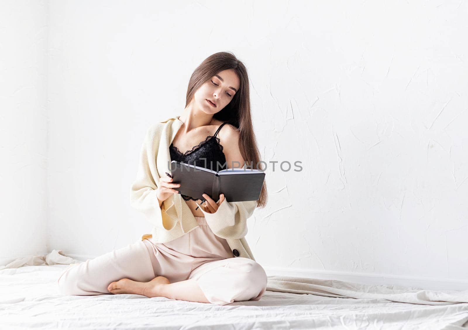 Beautiful sexy woman in comfy home clothes writing notes sitting on the floor, thinking