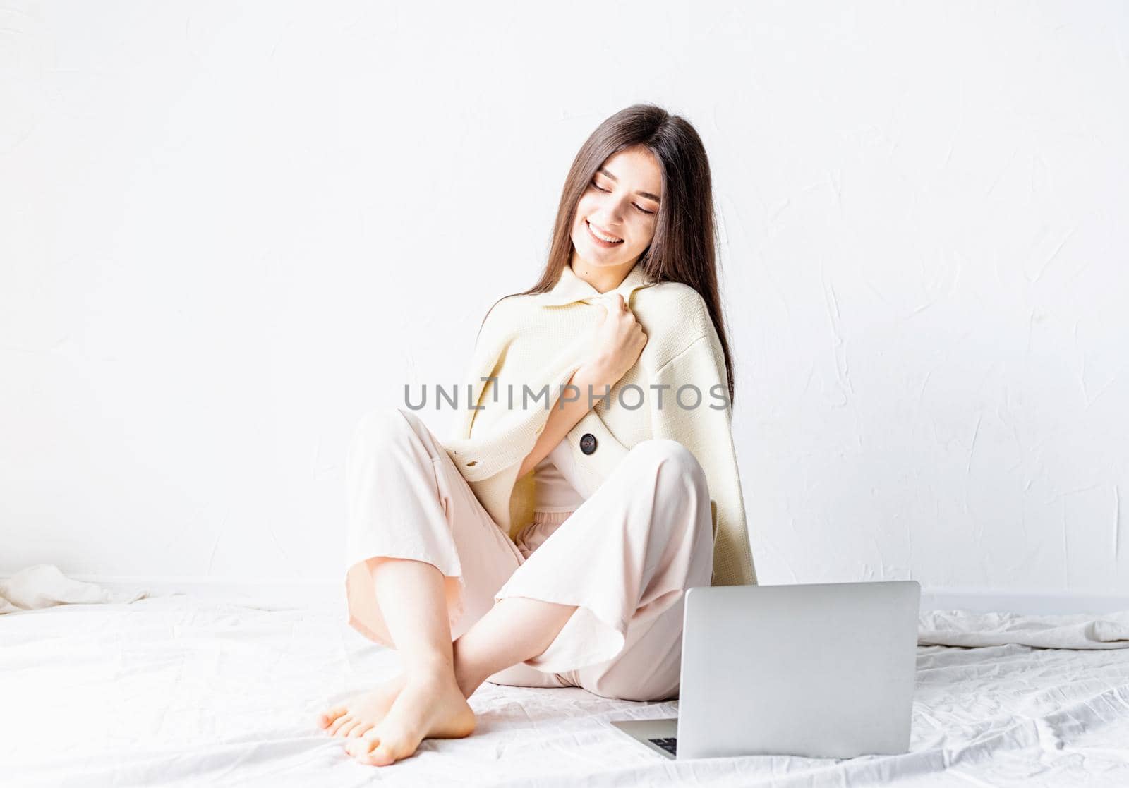 Beautiful young woman sitting on the floor and doing freelance project on laptop, using computer