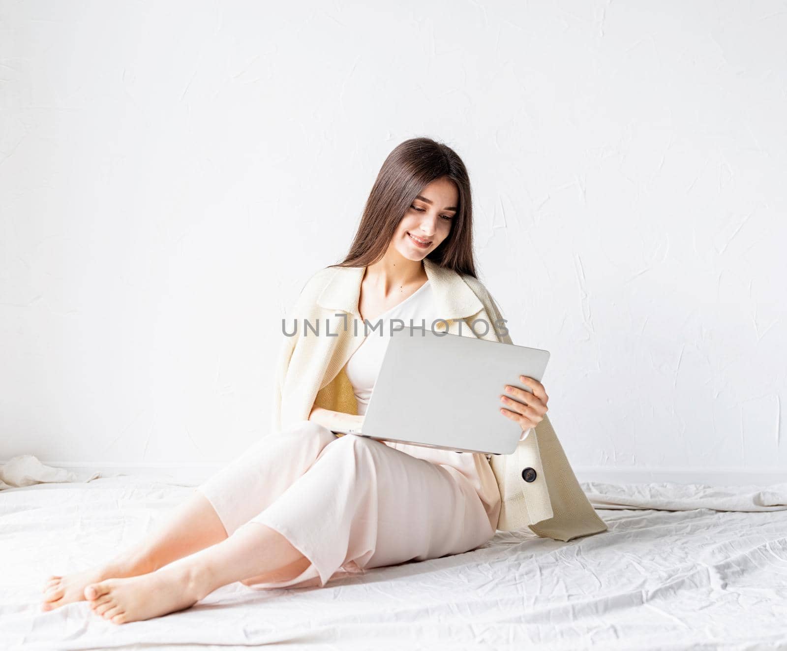 Beautiful smiling young woman sitting on the floor and doing freelance project on laptop, using computer