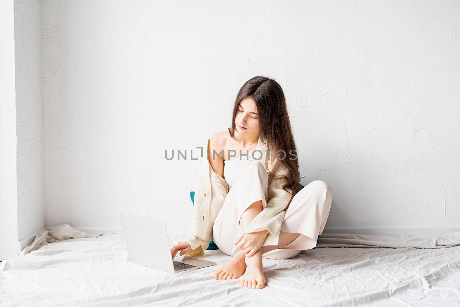 Beautiful young woman sitting on the floor and doing freelance project on laptop, using computer