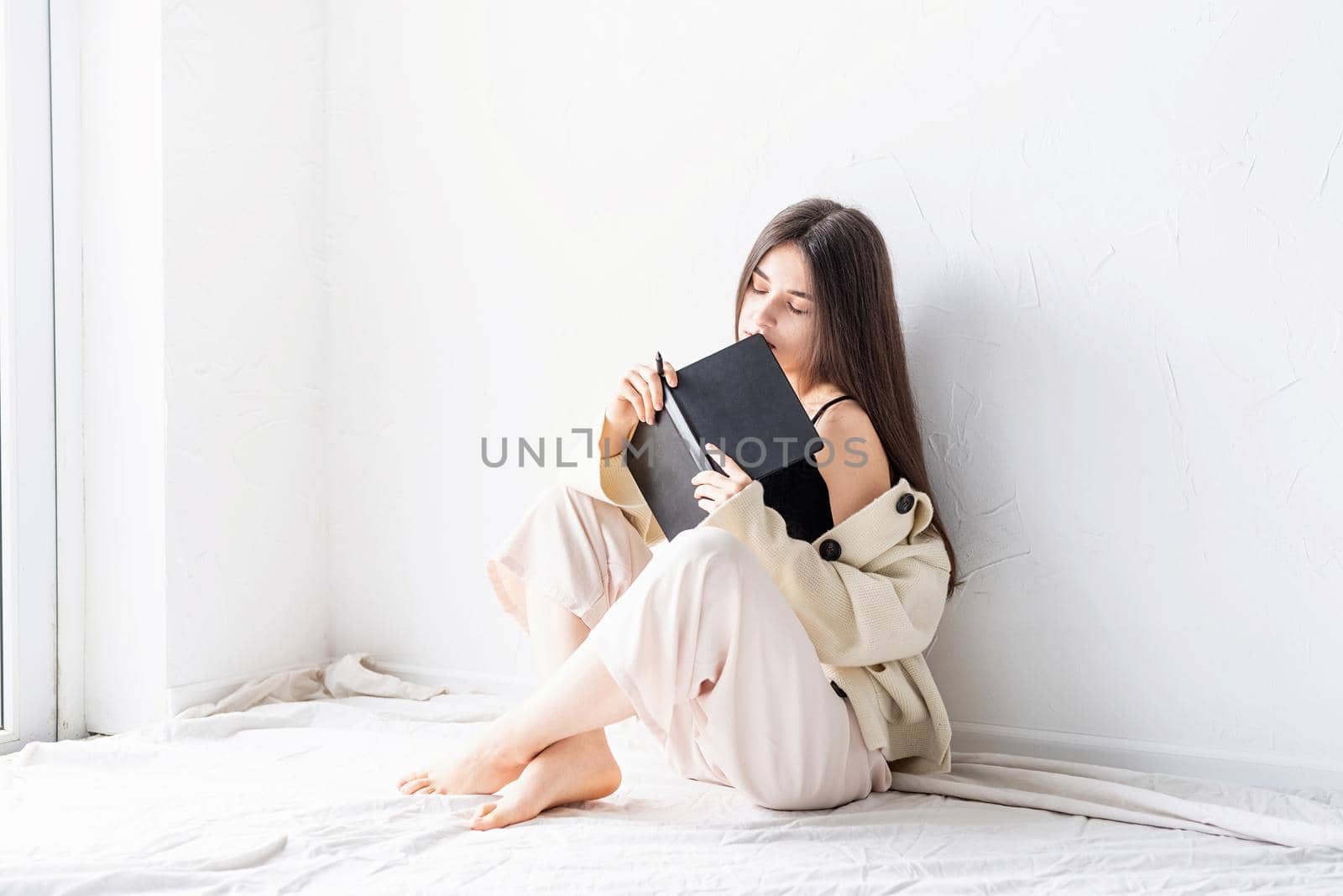 Beautiful sexy woman in comfy home clothes writing notes sitting on the floor, dreaming with eyes closed