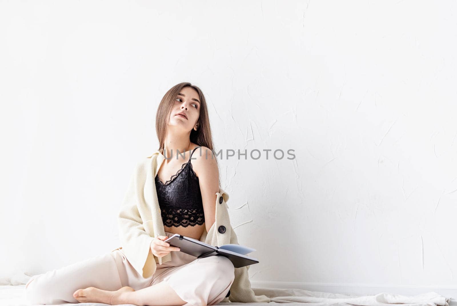 Beautiful sexy woman in comfy home clothes writing notes sitting on the floor, thinking