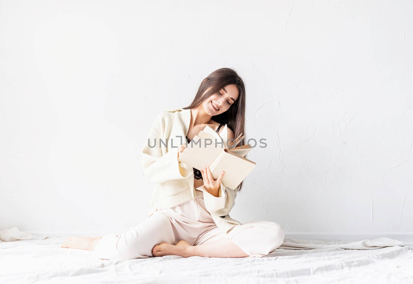 Beautiful smiling woman in comfortable home clothes reading a book sitting on the floor smiling