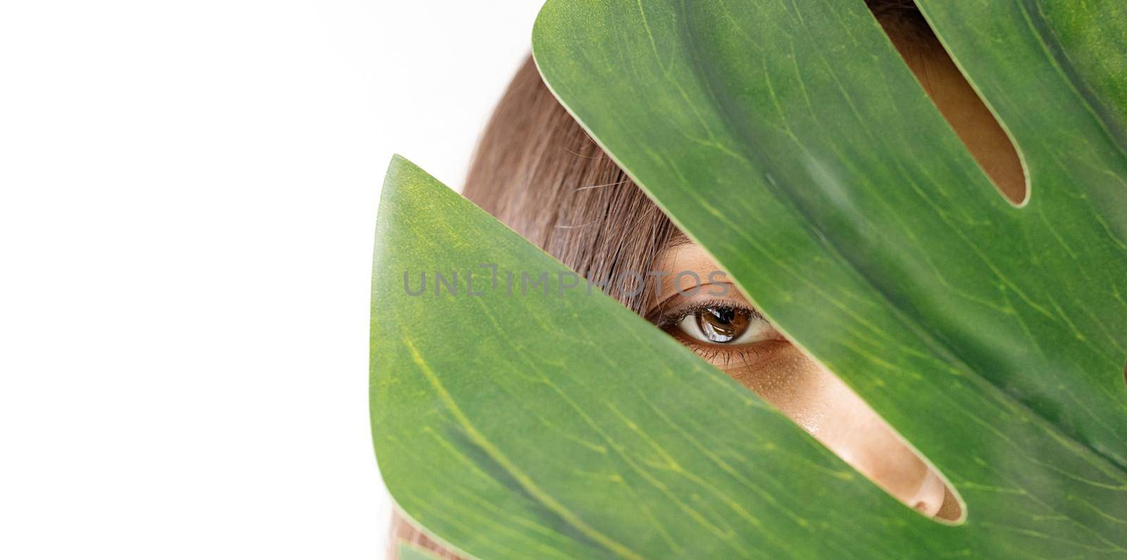 Happy beautiful woman in cozy clothes holding a green monstera leaf in front of her face by Desperada