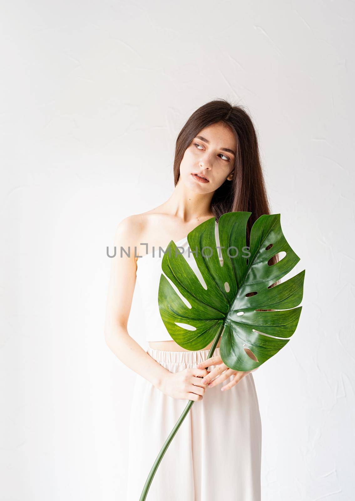 Happy beautiful woman in cozy clothes holding a green monstera leaf by Desperada